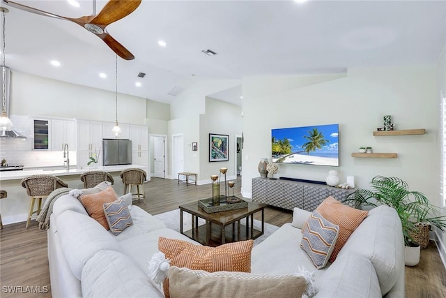 living room featuring light wood finished floors, high vaulted ceiling, ceiling fan, and baseboards