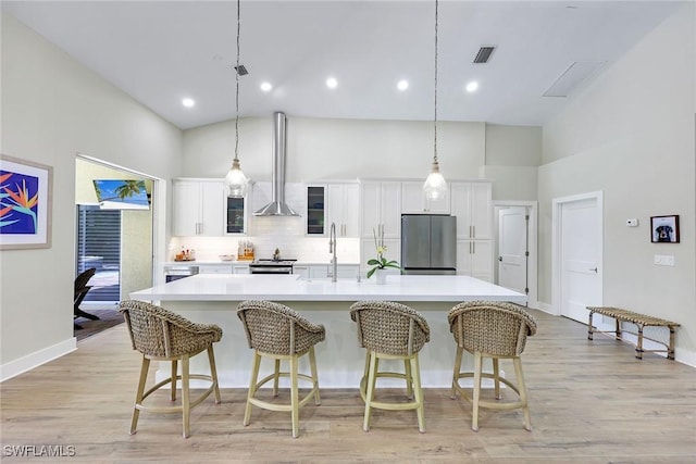 kitchen with a spacious island, appliances with stainless steel finishes, wall chimney range hood, visible vents, and high vaulted ceiling