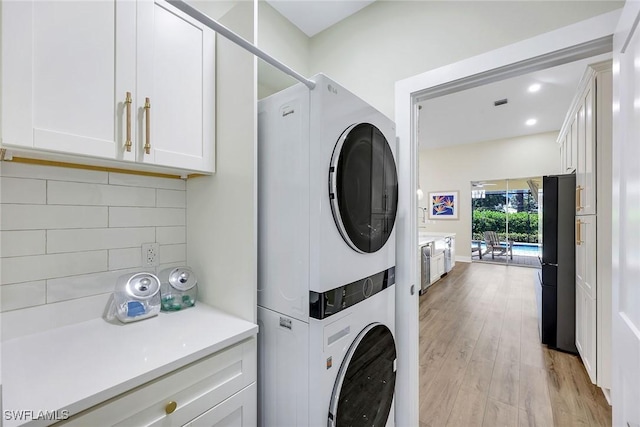 laundry area featuring recessed lighting, cabinet space, stacked washer and clothes dryer, and light wood-style floors