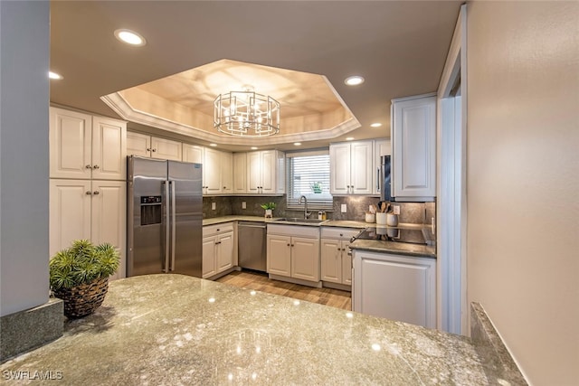 kitchen featuring a sink, tasteful backsplash, stainless steel appliances, and a tray ceiling