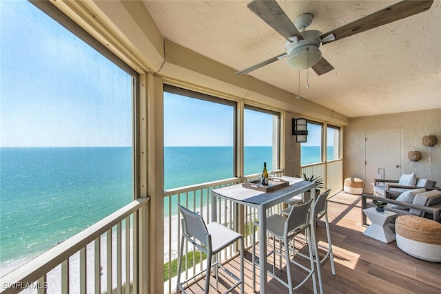 sunroom with a water view, a textured ceiling, wood finished floors, and a wealth of natural light