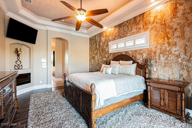 bedroom with crown molding, arched walkways, wood finished floors, baseboards, and a tray ceiling