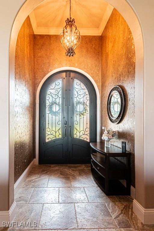 entrance foyer featuring an inviting chandelier, arched walkways, french doors, stone tile floors, and baseboards