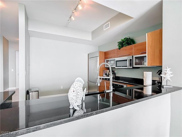 3000 Oasis Grand Blvd, Fort Myers, FL 33916 - kitchen featuring stainless steel microwave, brown cabinetry, rail lighting, visible vents, and a tray ceiling