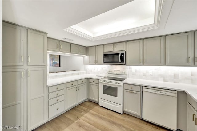 kitchen with white appliances, gray cabinets, tasteful backsplash, and a tray ceiling