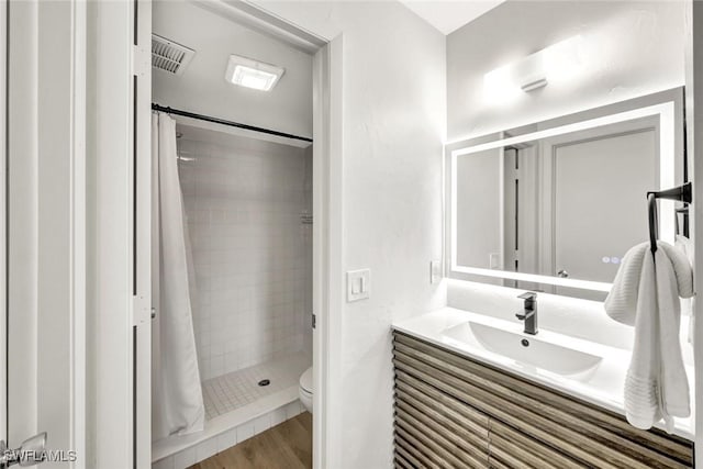 bathroom featuring a shower stall, toilet, vanity, and wood finished floors