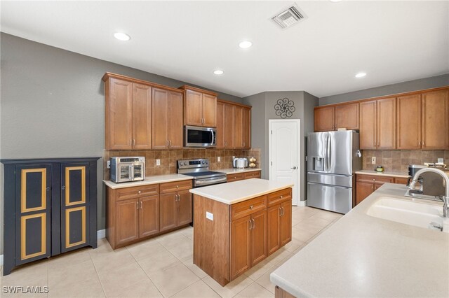 12869 Pastures Way, Fort Myers, FL 33913 - kitchen featuring appliances with stainless steel finishes, a kitchen island, tasteful backsplash, brown cabinets, and light countertops
