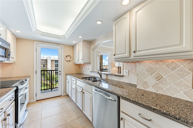 kitchen with stainless steel appliances, a sink, tasteful backsplash, dark stone counters, and a raised ceiling