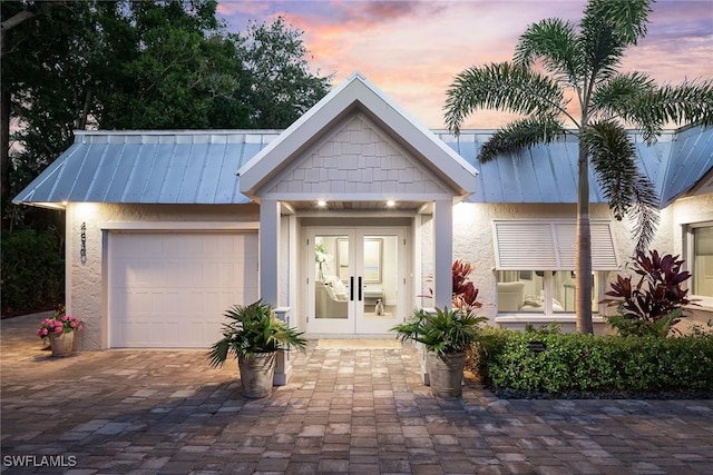4830 W Blvd, Naples, FL 34103 - view of front facade with french doors, an attached garage, a standing seam roof, driveway, and stucco siding