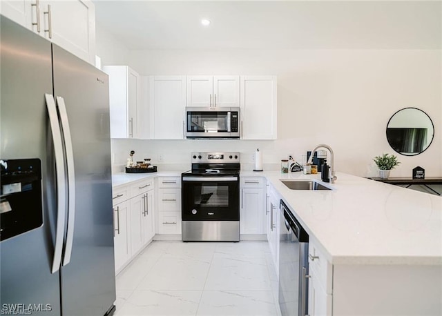kitchen featuring white cabinets, marble finish floor, stainless steel appliances, a sink, and a peninsula