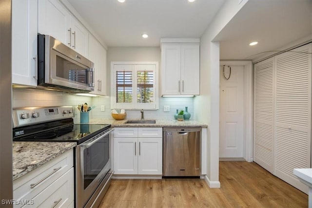 kitchen featuring white cabinetry, a sink, stainless steel appliances, light wood finished floors, and backsplash