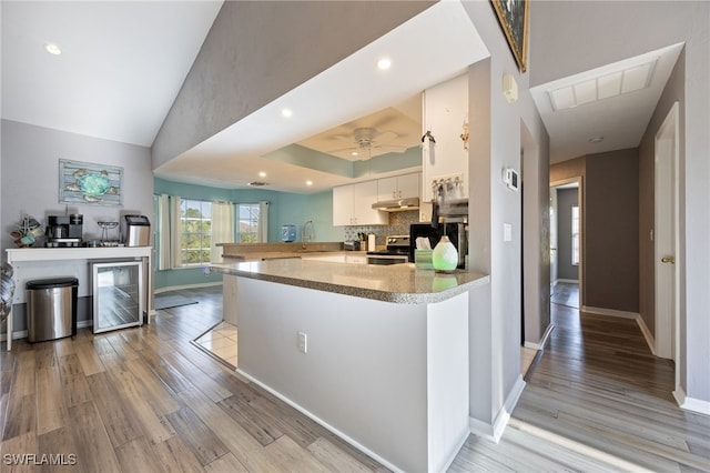 kitchen featuring stainless steel range with electric stovetop, under cabinet range hood, light wood-type flooring, a peninsula, and beverage cooler