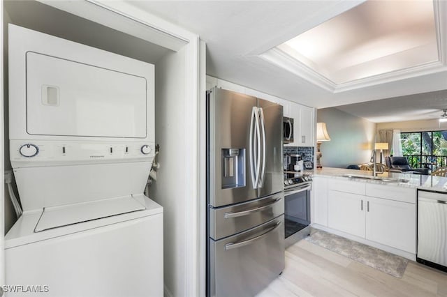 15177 Parkside Dr Unit 104, Fort Myers, FL 33908 - kitchen with white cabinetry, tasteful backsplash, light wood-style flooring, stacked washer and clothes dryer, and stainless steel appliances