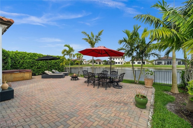 view of patio featuring a water view, outdoor dining space, an outdoor fire pit, fence, and a covered hot tub