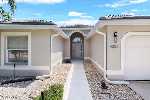 property entrance with stucco siding, a tile roof, and an attached garage