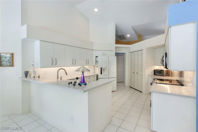 kitchen with light tile patterned floors, a peninsula, white refrigerator with ice dispenser, and stainless steel microwave
