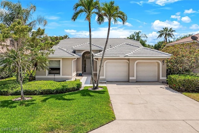 view of front of property with concrete driveway, a tile roof, an attached garage, stucco siding, and a front lawn