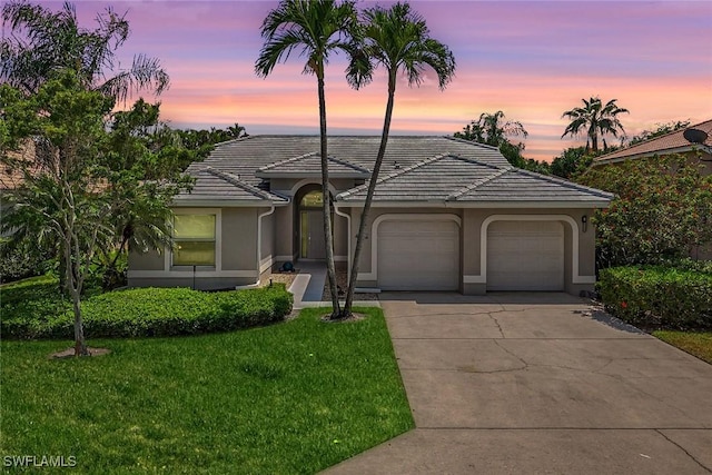 single story home featuring stucco siding, a tile roof, driveway, a front yard, and an attached garage