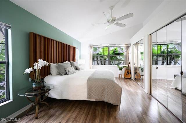 bedroom featuring lofted ceiling, ceiling fan, baseboards, wood finished floors, and multiple closets