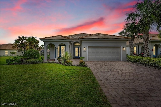 mediterranean / spanish house featuring a tile roof, a yard, stucco siding, decorative driveway, and an attached garage