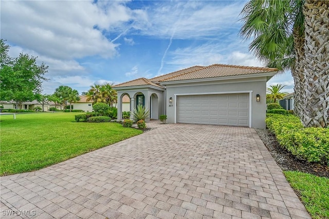 mediterranean / spanish-style home featuring a tile roof, decorative driveway, an attached garage, stucco siding, and a front lawn