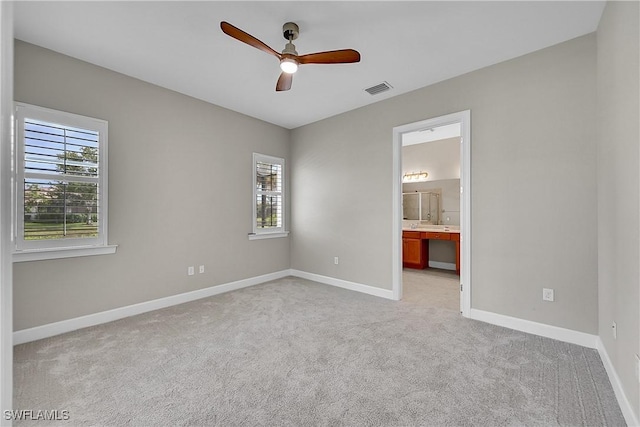 unfurnished bedroom with light colored carpet, ceiling fan, ensuite bathroom, baseboards, and visible vents