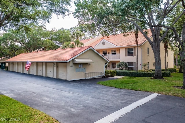 view of front of home featuring a tile roof, community garages, a front yard, and stucco siding