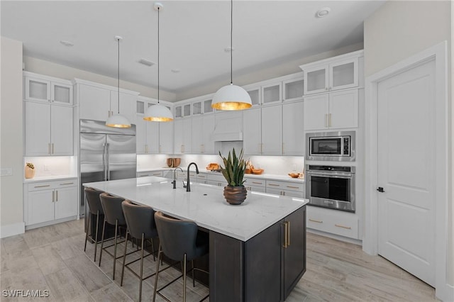 16198 Verilyn Cir, Naples, FL 34110 - kitchen featuring built in appliances, white cabinets, light wood-style floors, a large island, and decorative light fixtures