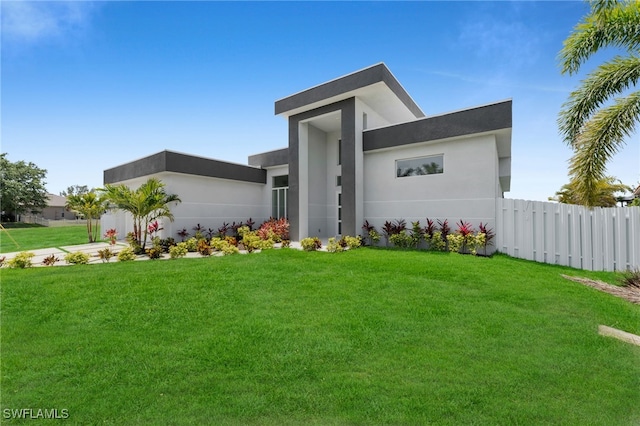 view of front of house featuring fence, a front lawn, and stucco siding