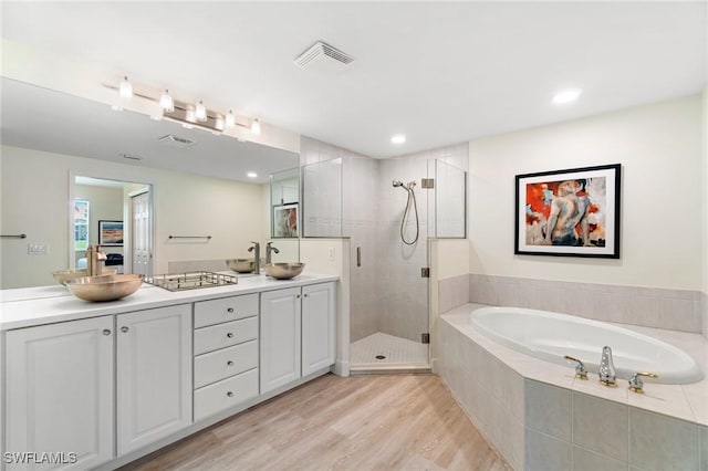 ensuite bathroom with double vanity, wood finished floors, visible vents, a garden tub, and a stall shower