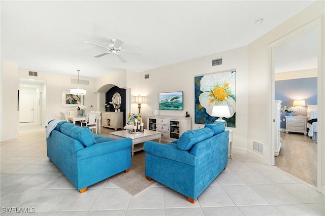 living room featuring visible vents, a ceiling fan, arched walkways, and light tile patterned flooring