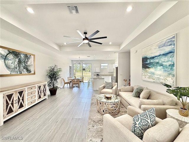 living area featuring a raised ceiling, visible vents, recessed lighting, light wood finished floors, and a ceiling fan