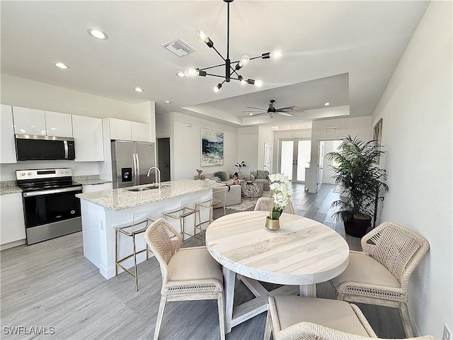 dining room with a raised ceiling, visible vents, light wood-type flooring, recessed lighting, and a notable chandelier