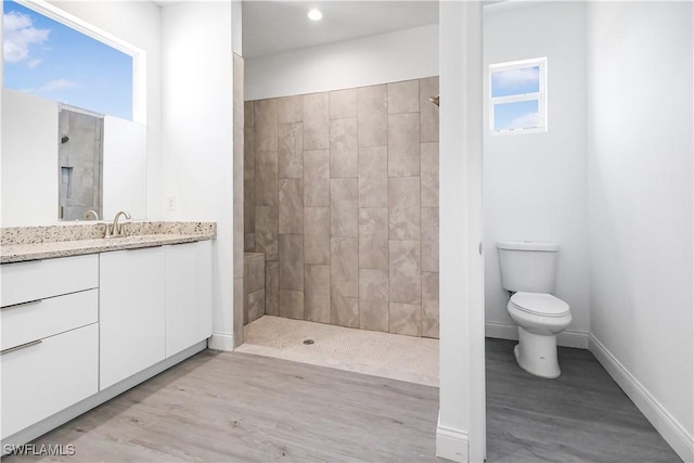 full bathroom featuring baseboards, wood finished floors, a tile shower, and vanity