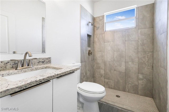 full bathroom featuring toilet, a tile shower, and vanity