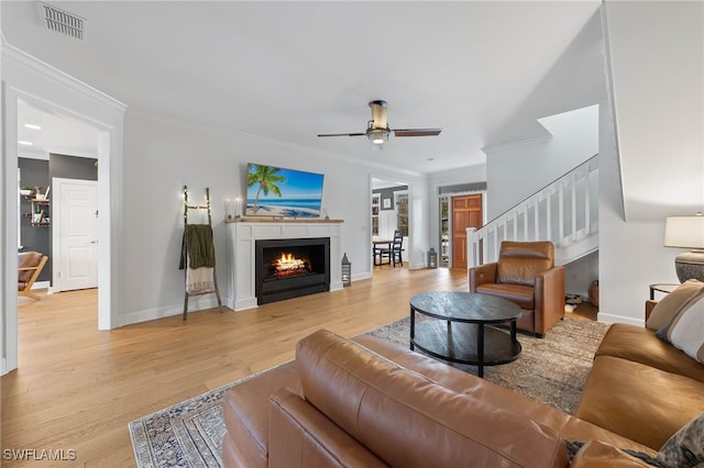 living area featuring visible vents, ornamental molding, baseboards, ceiling fan, and light wood-style flooring
