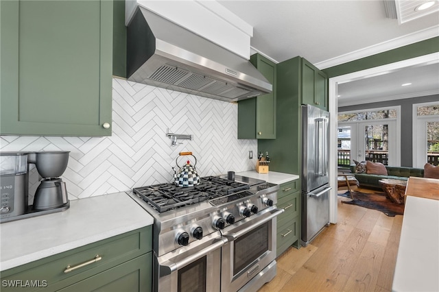 kitchen with crown molding, high quality appliances, light countertops, wall chimney exhaust hood, and green cabinets