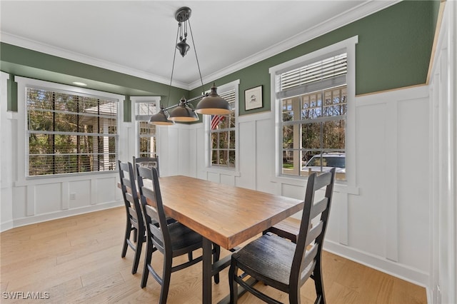 dining room with ornamental molding, a wainscoted wall, light wood finished floors, and a decorative wall