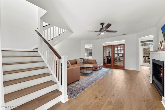 living area featuring a ceiling fan, visible vents, wood-type flooring, ornamental molding, and stairs