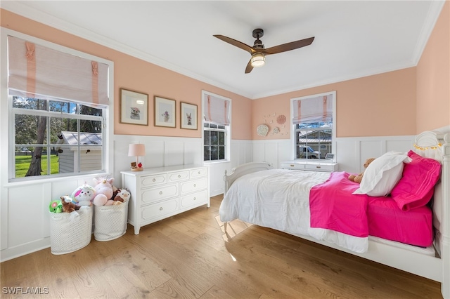 bedroom featuring crown molding, ceiling fan, wainscoting, and light wood-type flooring
