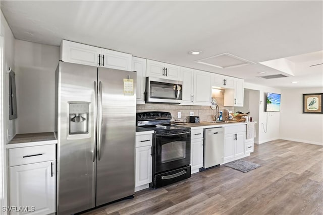 kitchen featuring decorative backsplash, wood finished floors, light countertops, white cabinetry, and appliances with stainless steel finishes