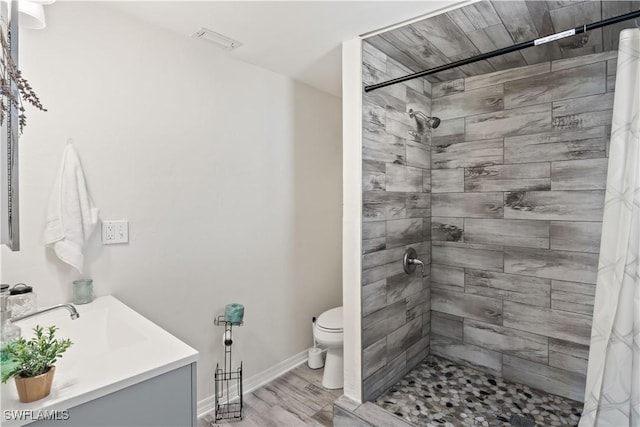 bathroom with a tile shower, wood finished floors, vanity, baseboards, and toilet