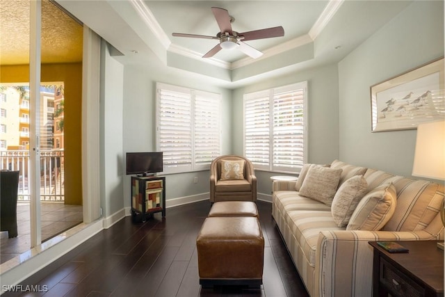 living room featuring ornamental molding, baseboards, a raised ceiling, a ceiling fan, and dark wood-type flooring
