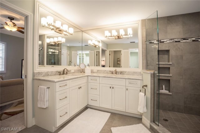 bathroom with tiled shower, ceiling fan with notable chandelier, double vanity, and a sink