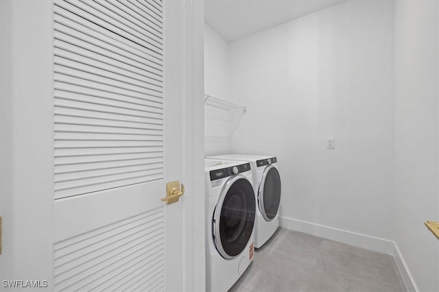 clothes washing area with light tile patterned floors, washing machine and clothes dryer, laundry area, and baseboards
