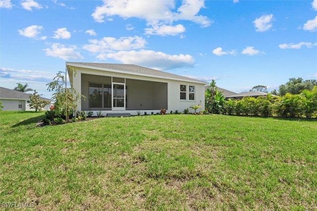 rear view of house featuring a lawn, stucco siding, and a sunroom