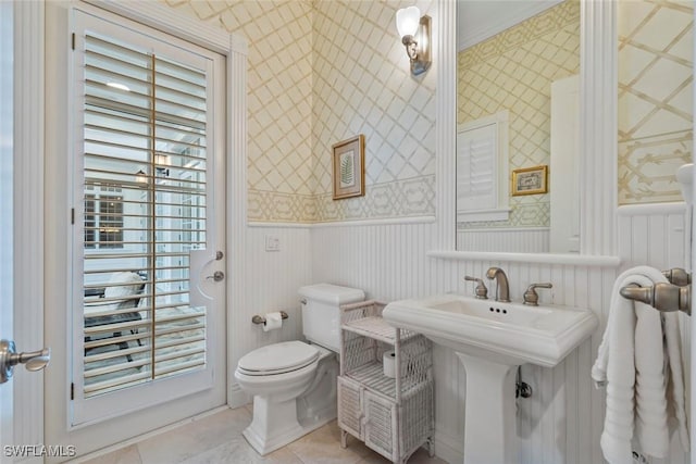 half bath featuring wainscoting, a sink, tile patterned floors, toilet, and wallpapered walls