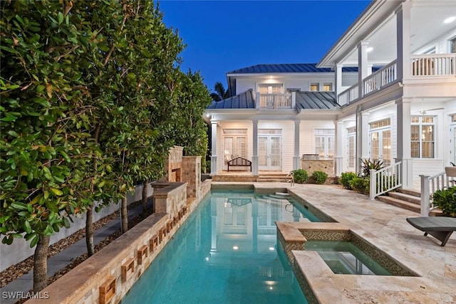 rear view of property featuring french doors, an in ground hot tub, a balcony, a standing seam roof, and metal roof