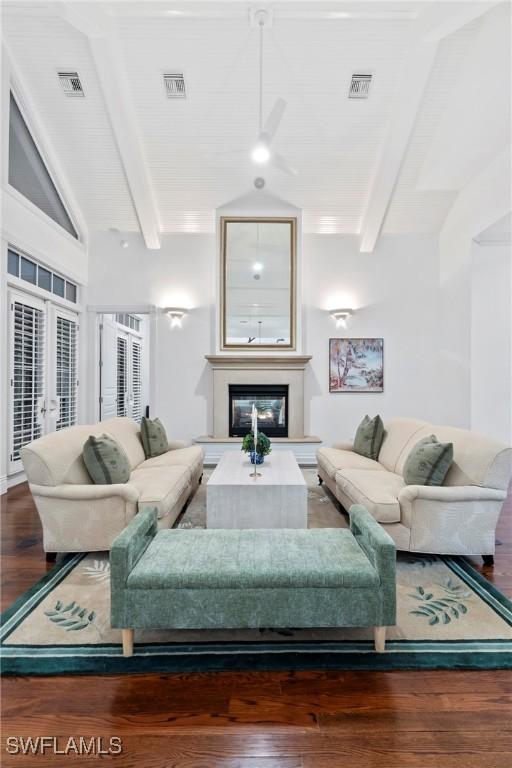 living area featuring visible vents, a glass covered fireplace, wood finished floors, and vaulted ceiling with beams