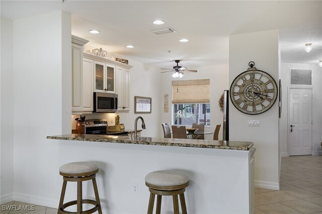 kitchen featuring appliances with stainless steel finishes, a breakfast bar, visible vents, and dark stone countertops